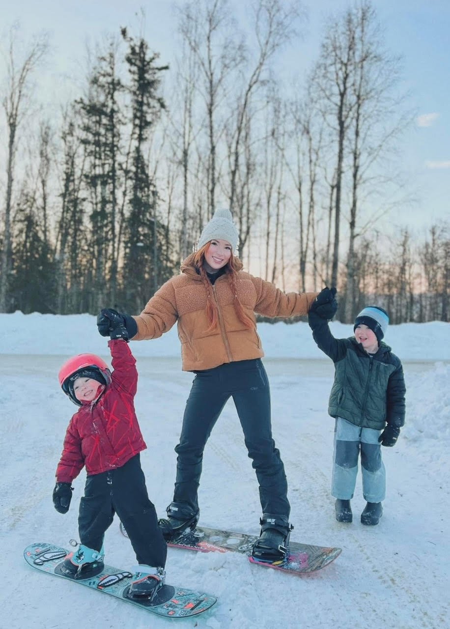 Mother and two children snowboarding together in the Alaska winter